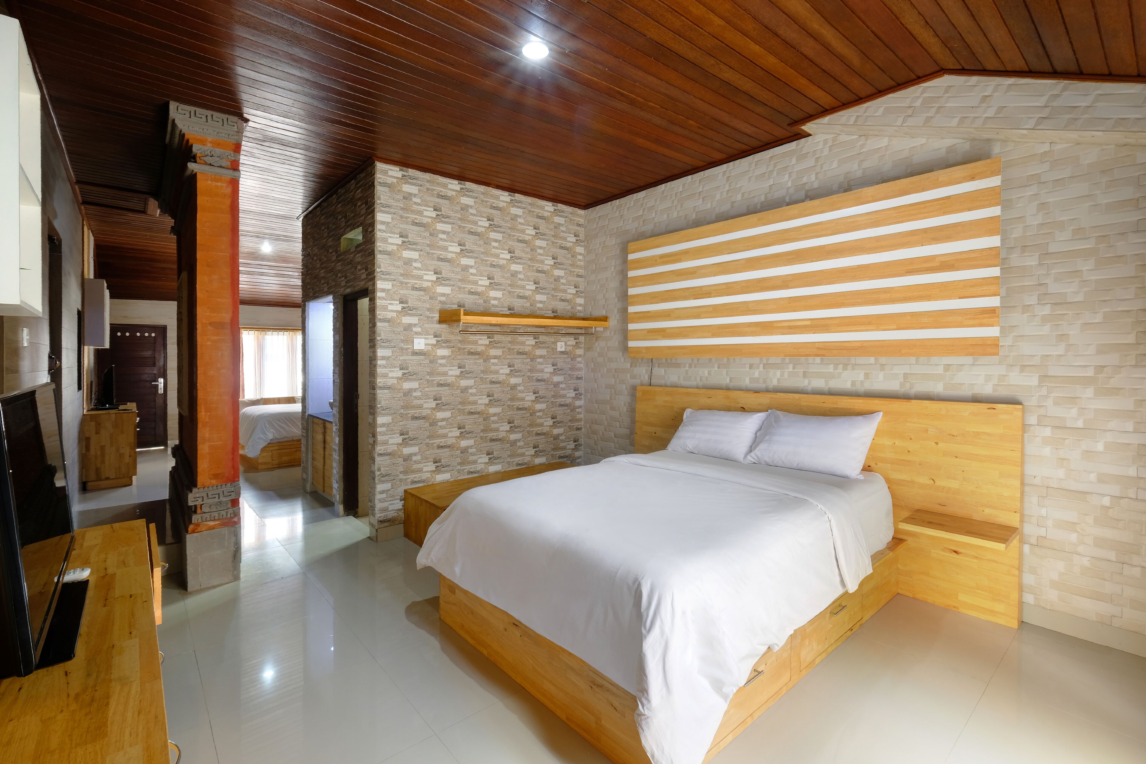 A modern bedroom with a wooden bed, a stone wall, and a wooden ceiling.