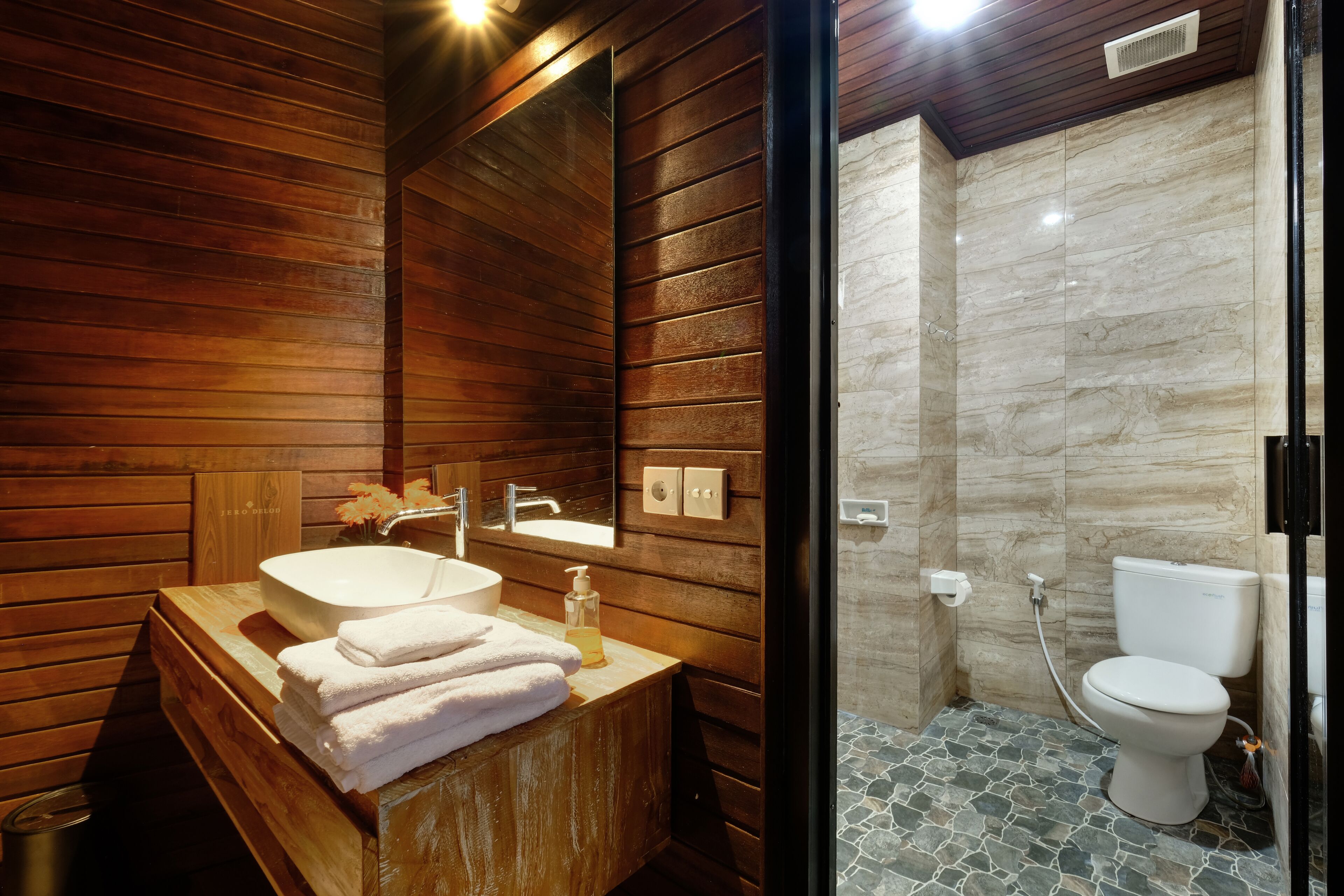 Un baño moderno con paneles de madera, un tocador de madera con lavamanos y cabina de ducha con mampara de vidrio.