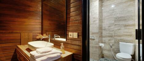 Un baño moderno con paneles de madera, un tocador de madera con lavamanos y cabina de ducha con mampara de vidrio.