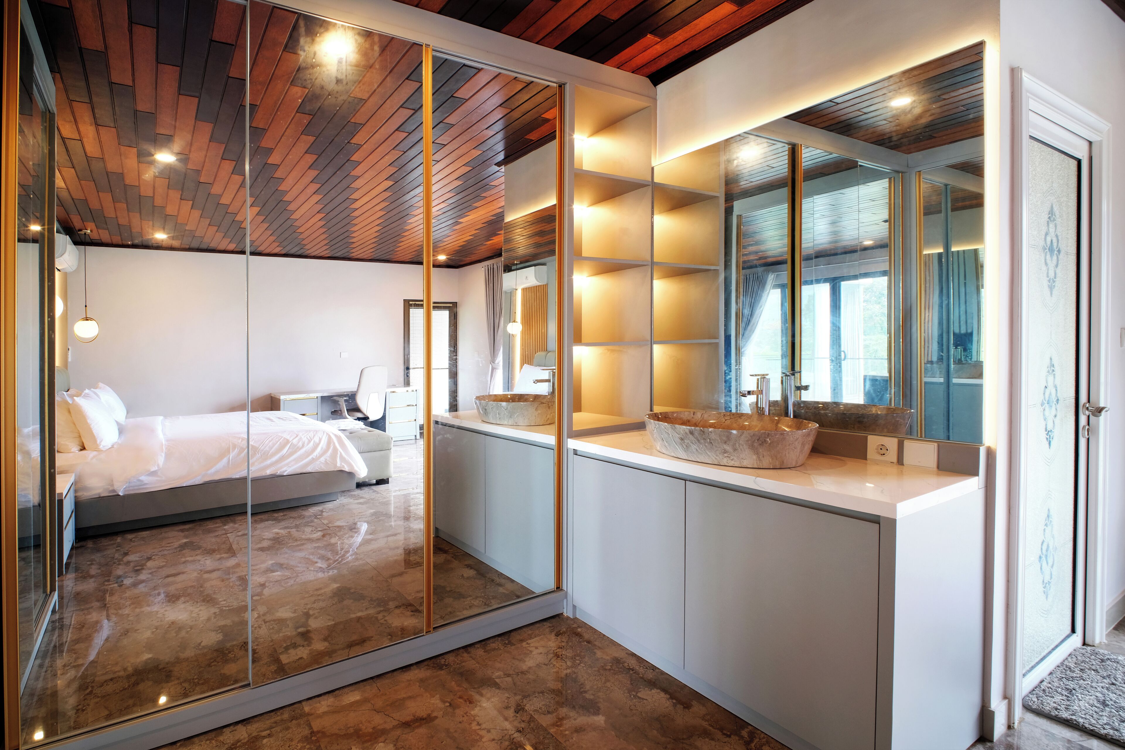 A modern bedroom with a glass partition, a large mirror, a wooden ceiling, and a white bedside table.