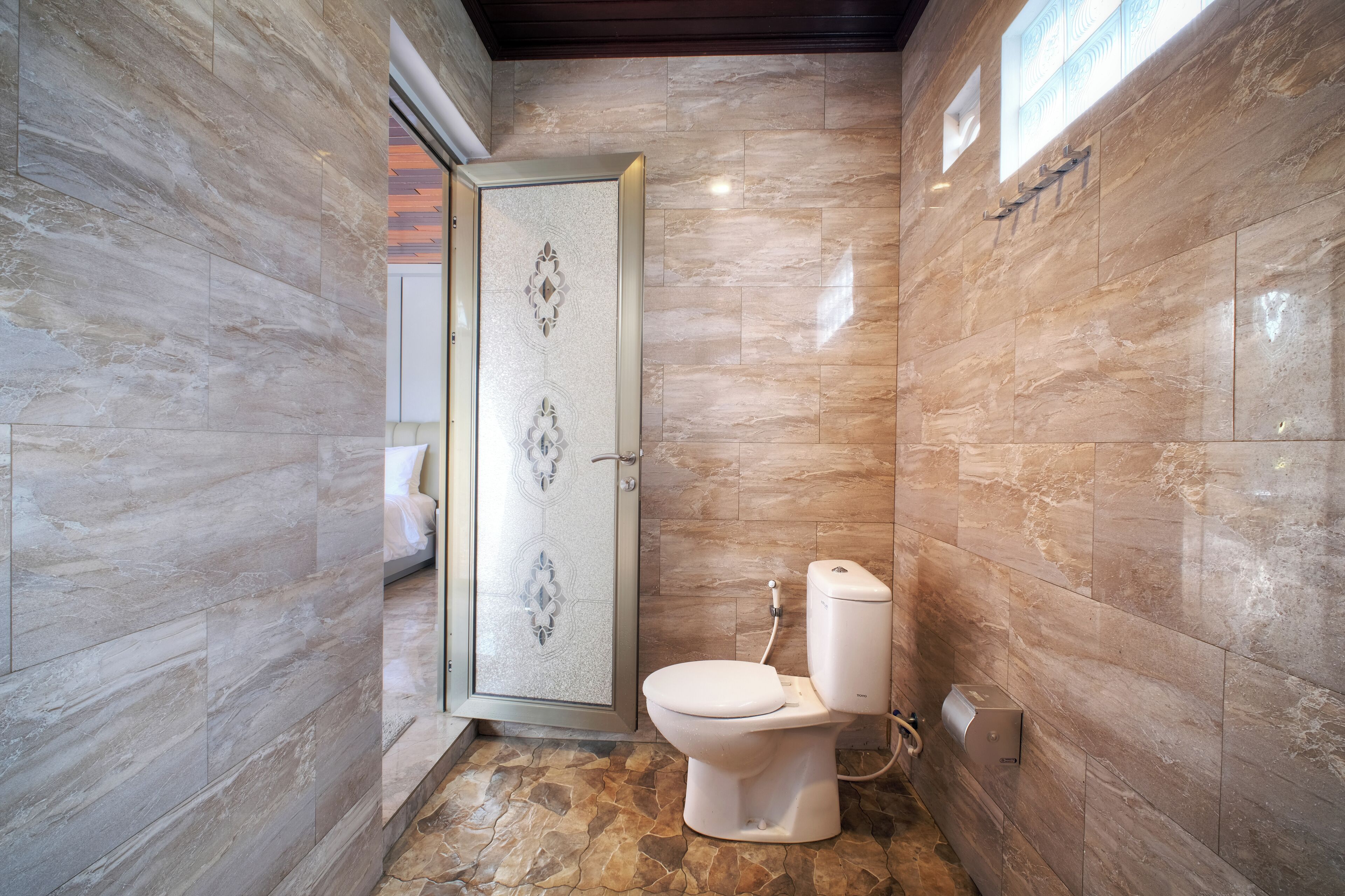 Un baño con inodoro, ducha con puerta de cristal y paredes de mármol.