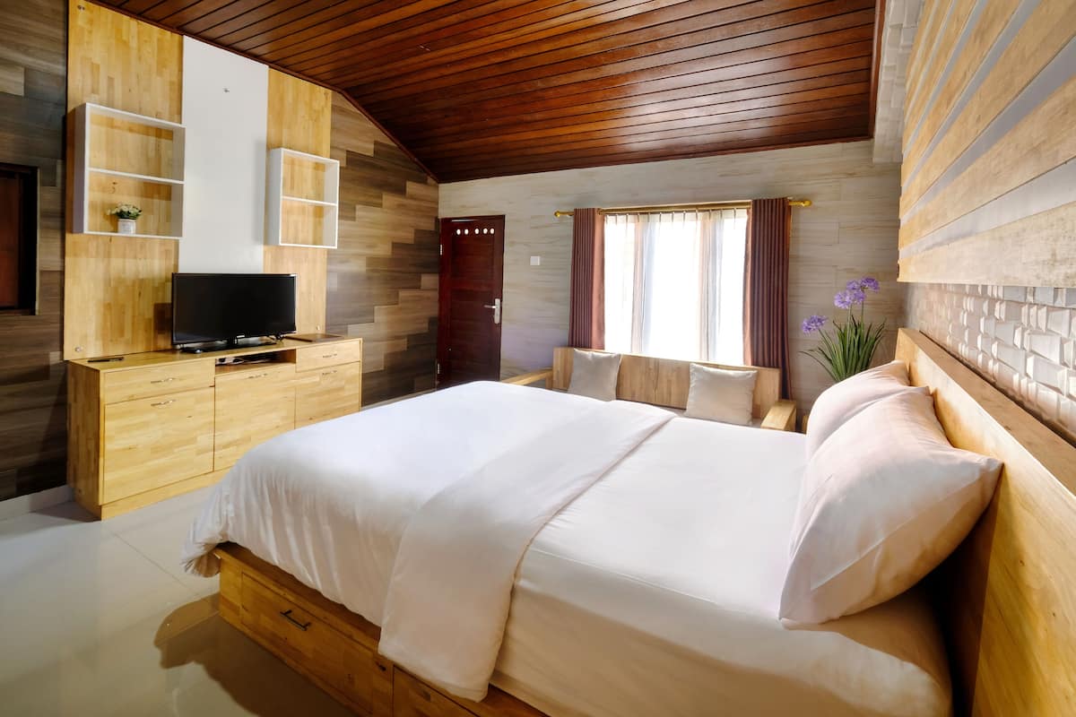 A bedroom with a wooden bed, a TV on a wooden cabinet, and a window with curtains.