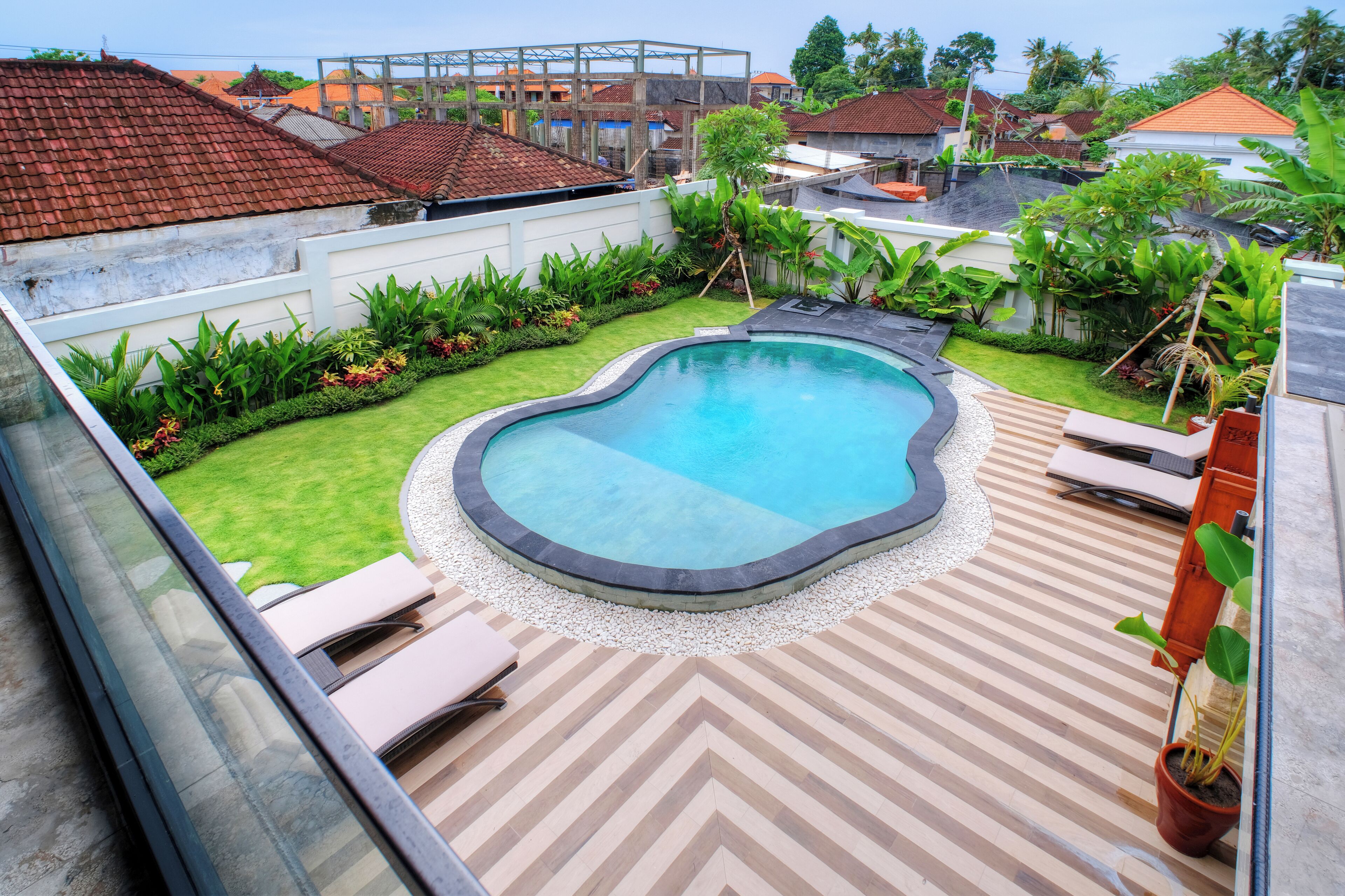 Une piscine entourée d’un jardin, avec une terrasse dont le revêtement est disposé en motif de chevrons.