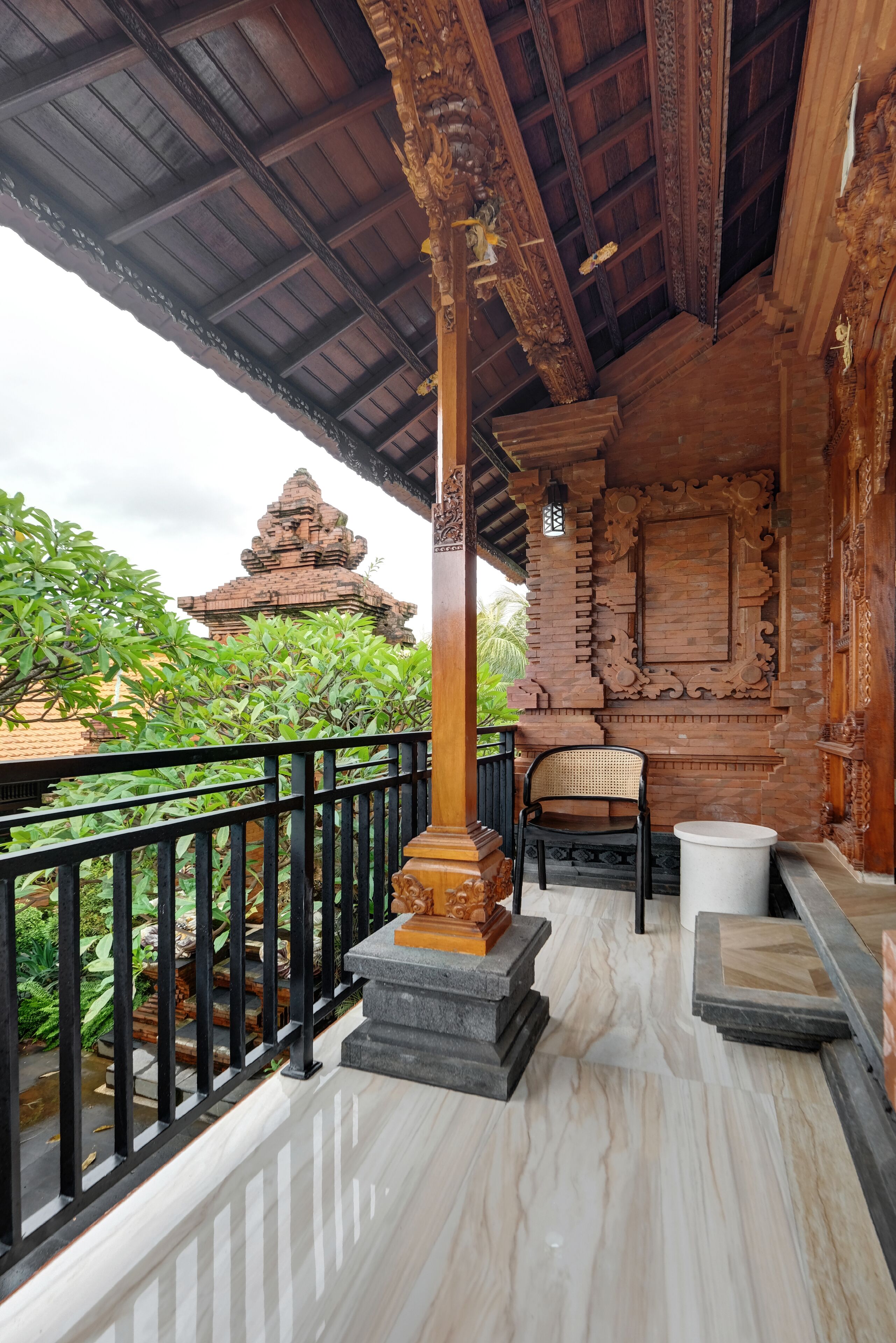 A wooden balcony with a tiled floor, a black chair, and a white trash bin.