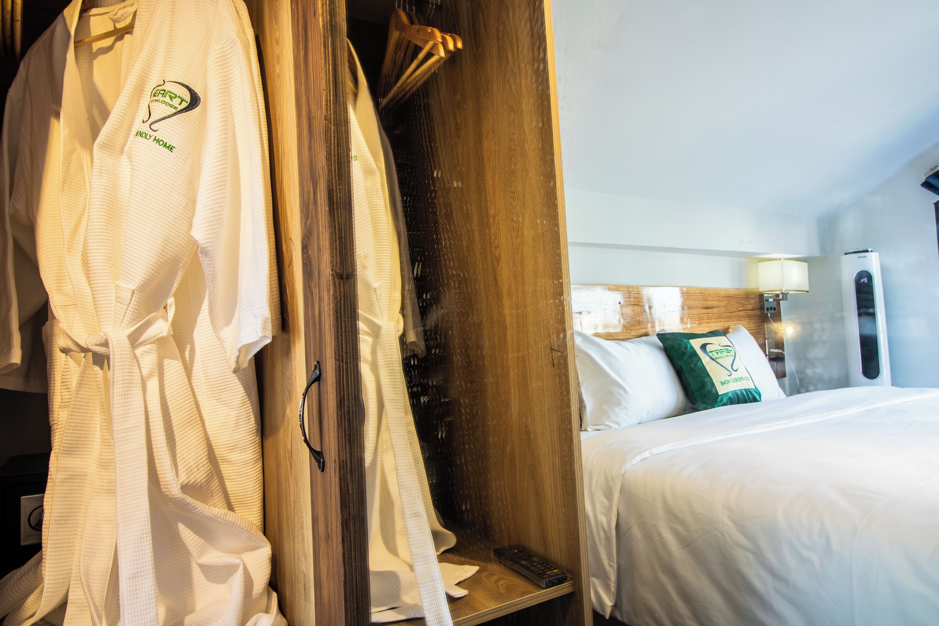 A hotel room with a wooden wardrobe, a bed with white bedding, and a robe hanging on the wardrobe.