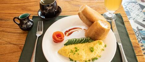 A breakfast plate with an omelet, bread, and vegetables on a wooden table.