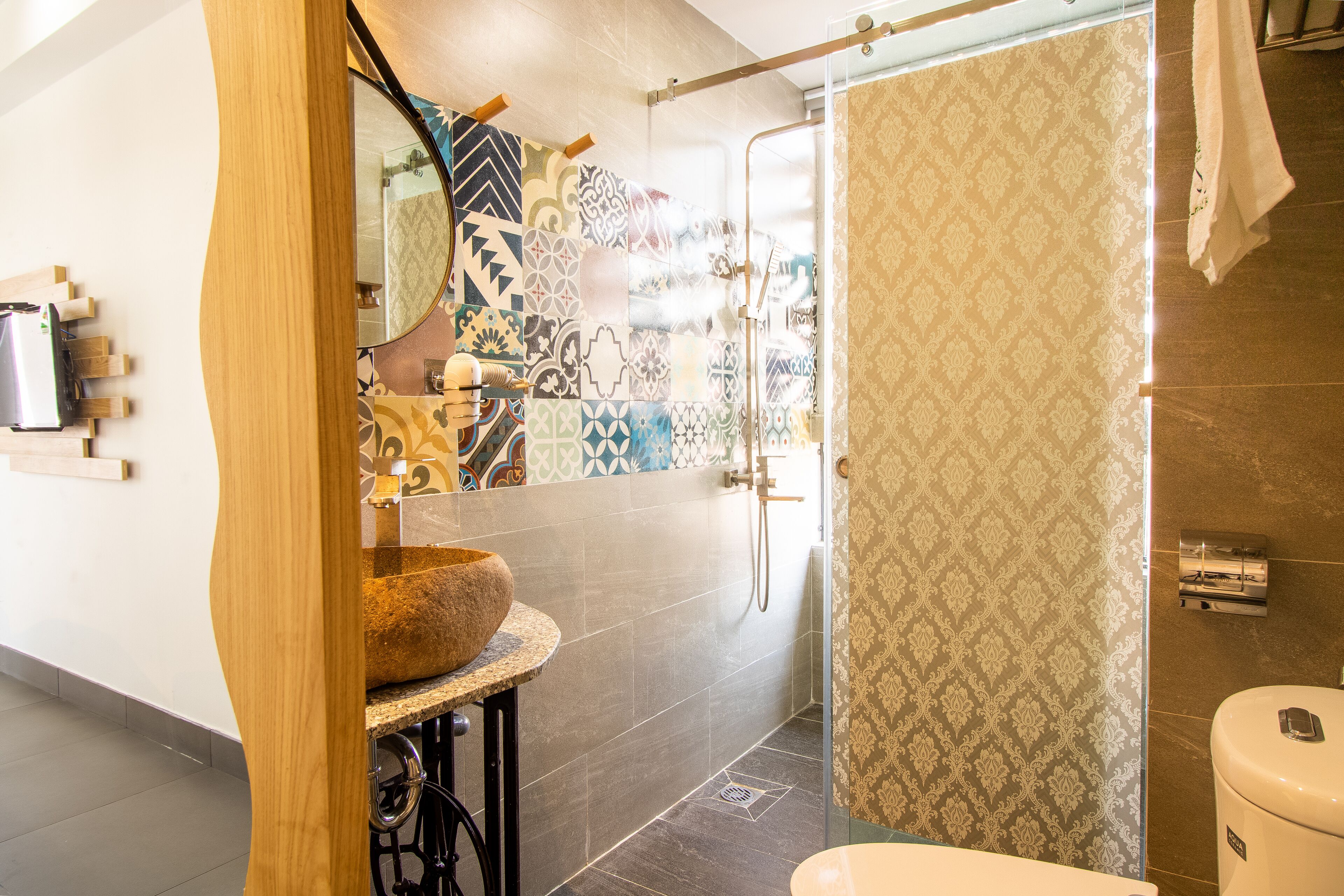 A modern bathroom with a stone sink, a shower with a glass door, and patterned tiles on the walls.