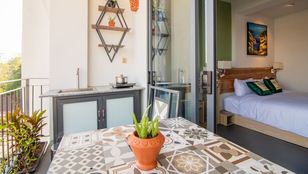 Un balcón con mesa, plantas en macetas y una cama con vistas al exterior.