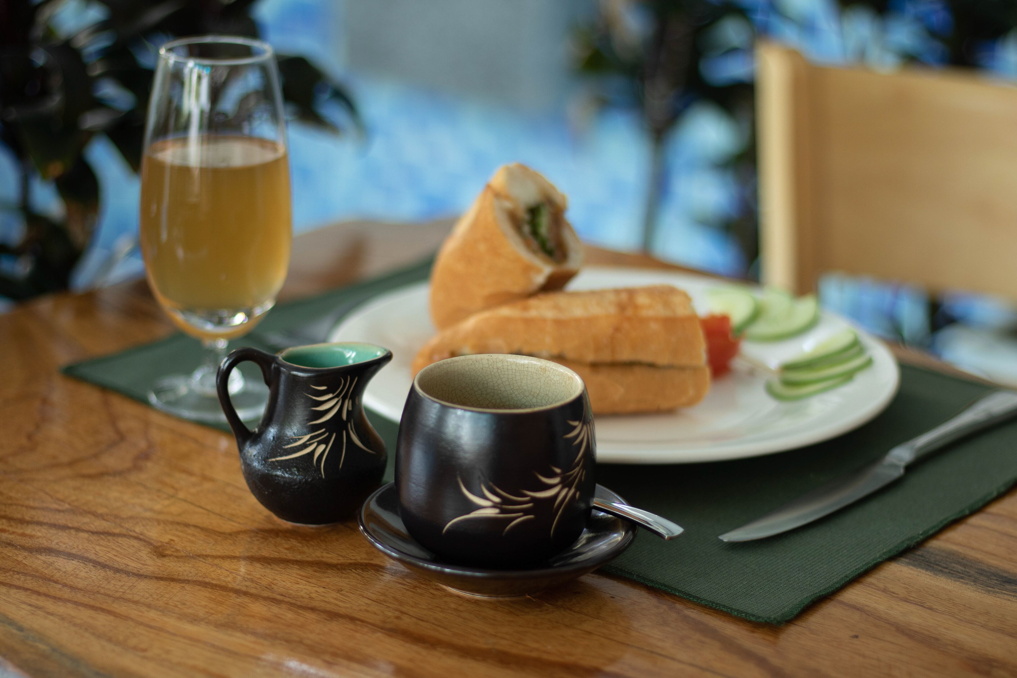 A table with a sandwich, a glass of drink, and two cups with a leaf design.
