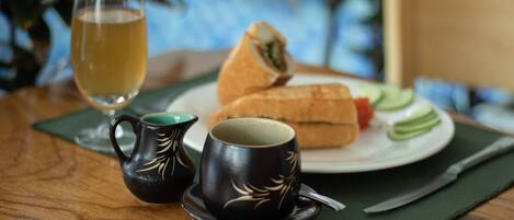 A table with a sandwich, a glass of drink, and two cups with a leaf design.