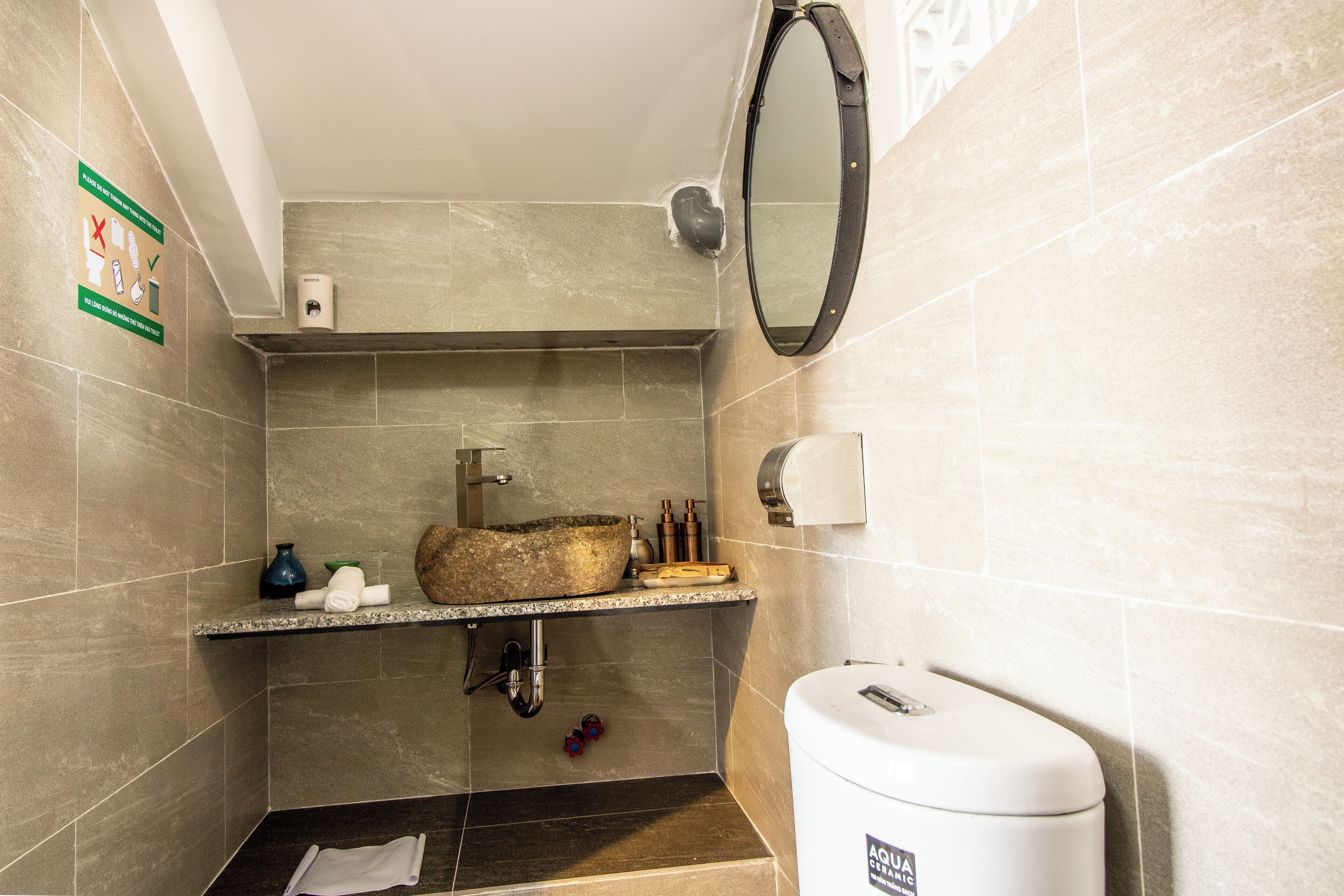 A bathroom with a stone sink, a mirror, a toilet, and a towel rack.