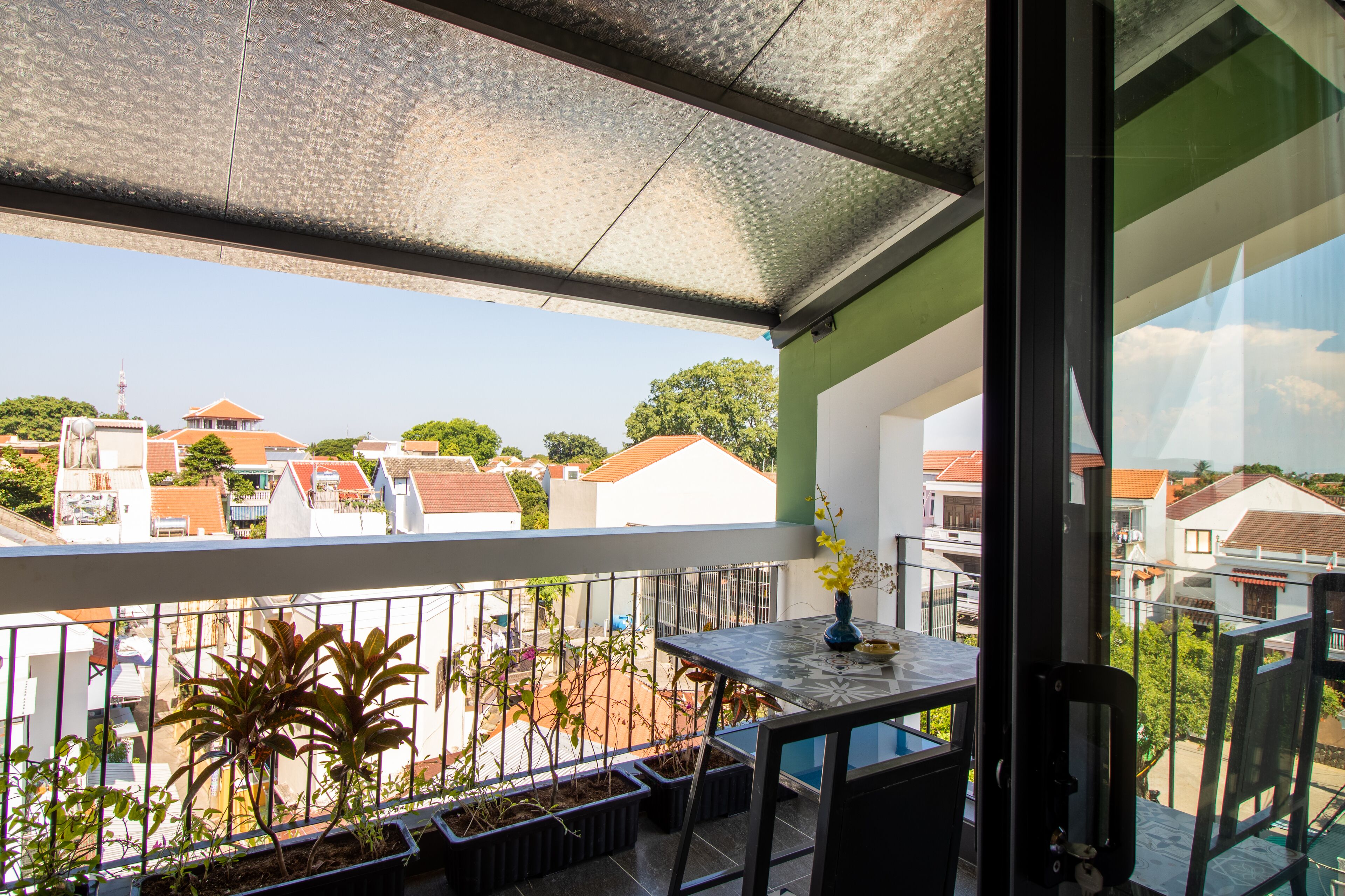 A balcony with a view of neighboring houses, a table with a vase, and potted plants.