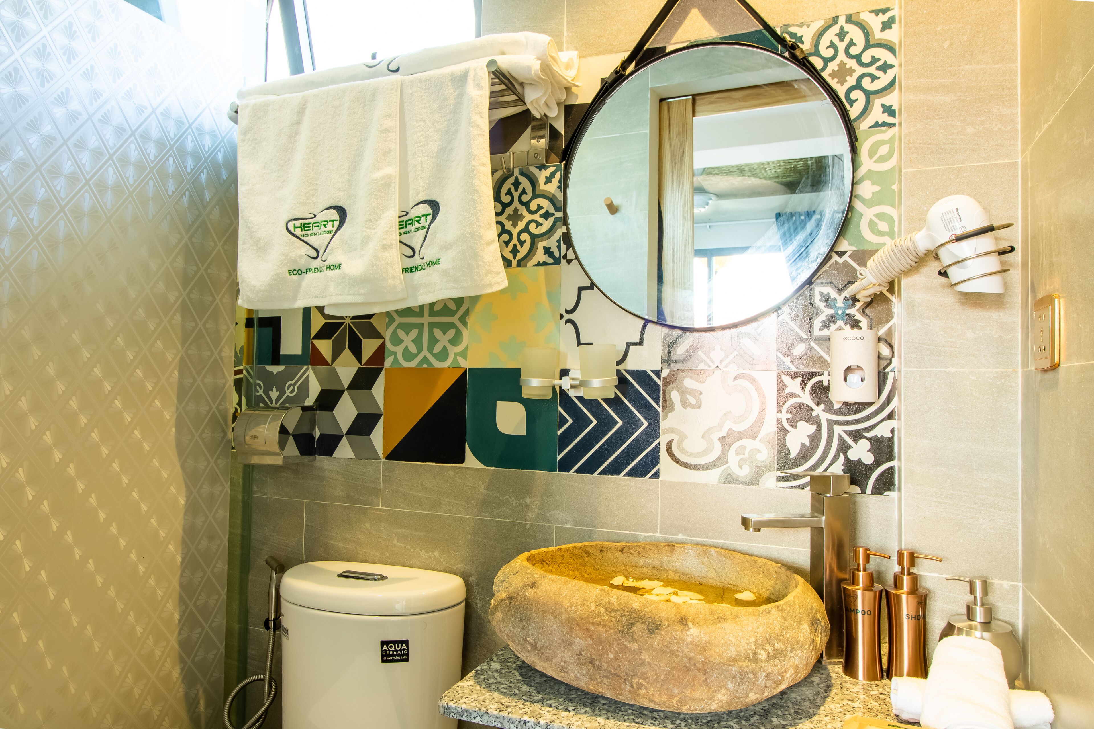 A bathroom with a stone sink, a toilet, a mirror, and a towel rack with a towel.