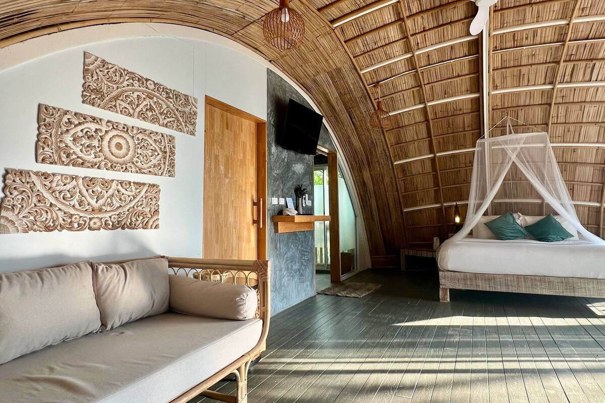 A room with a curved ceiling, a wooden bed with a canopy, a sofa, and decorative wall panels.