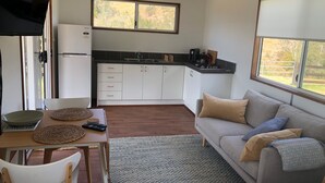 Una cucina compatta con mobili bianchi, un tavolo da pranzo con sottovaso in fibra naturale e un divano grigio con cuscini.