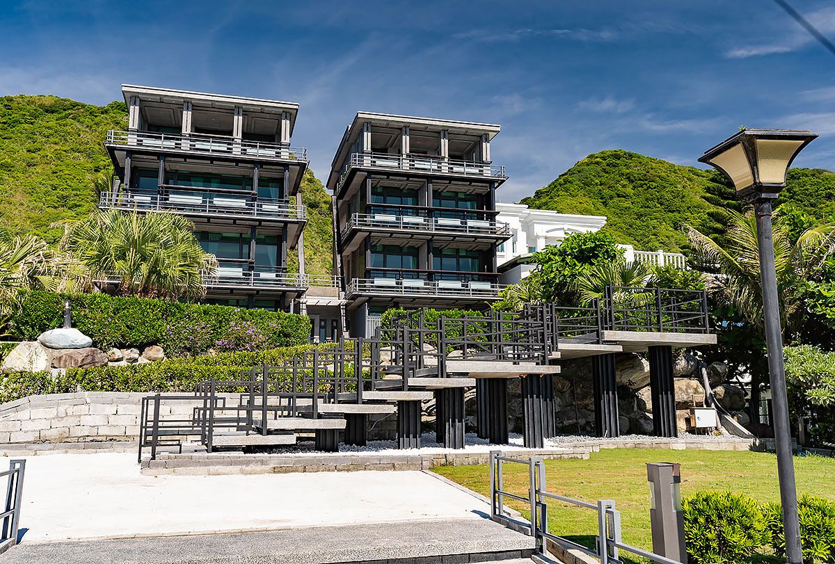 Et moderne hotel med flere etager, udendørs trapper og en frodig, grøn bakgrund.