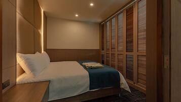 A hotel room with a bed, wooden headboard, and a large window with blinds.