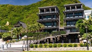A modern multi-story building with balconies, surrounded by lush greenery and a statue. - Seaview Villa Coastal Estate (Shoufeng)