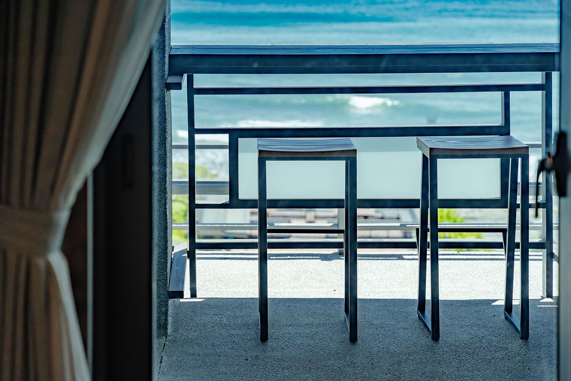 A balcony with two metal tables and chairs, overlooking a body of water.