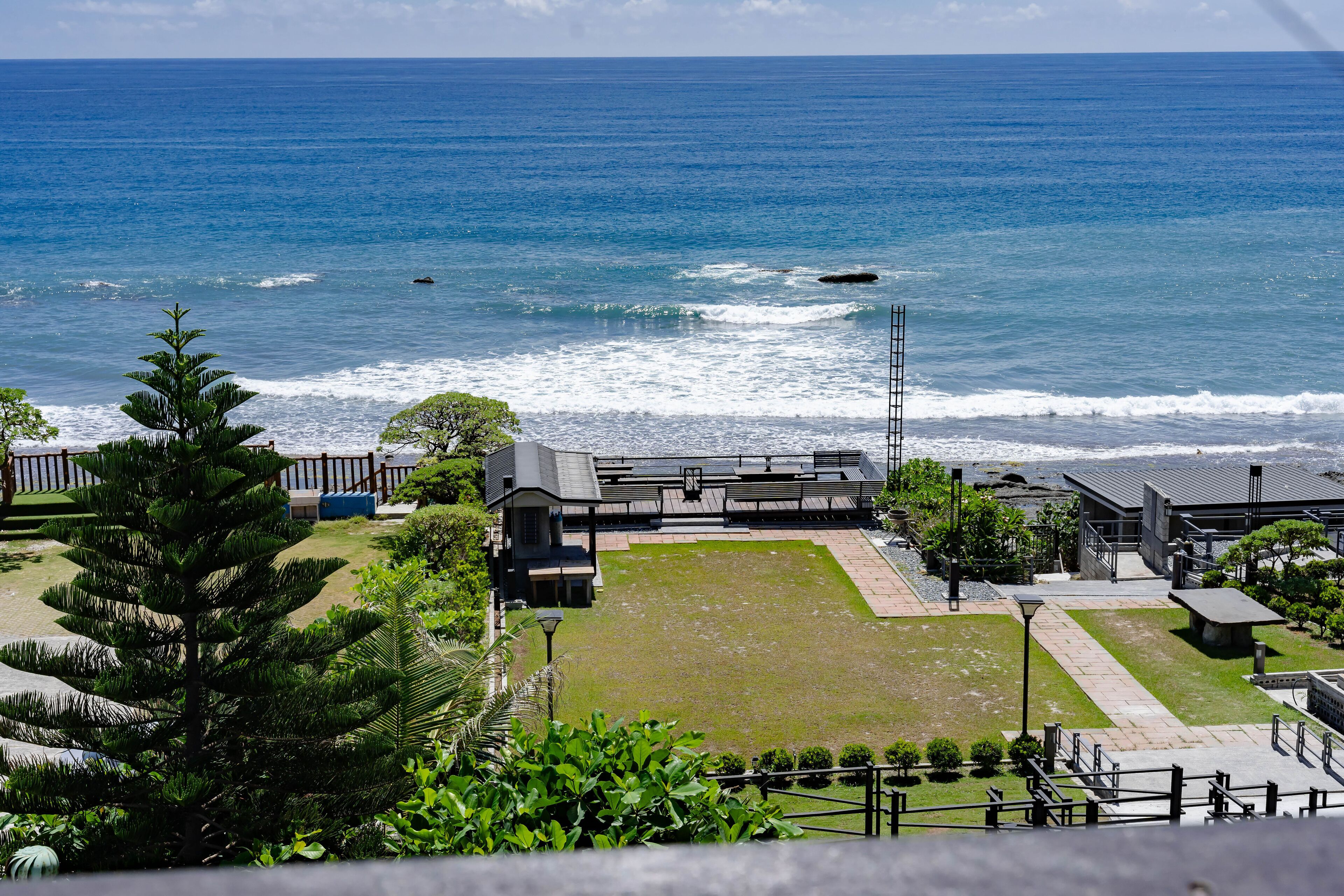 A coastal view with a building complex, including a parking area and a grassy lawn.