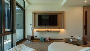 A modern hotel room with a large window, a flat-screen TV mounted on the wall, a sofa, a small round table, and decorative animal figures.