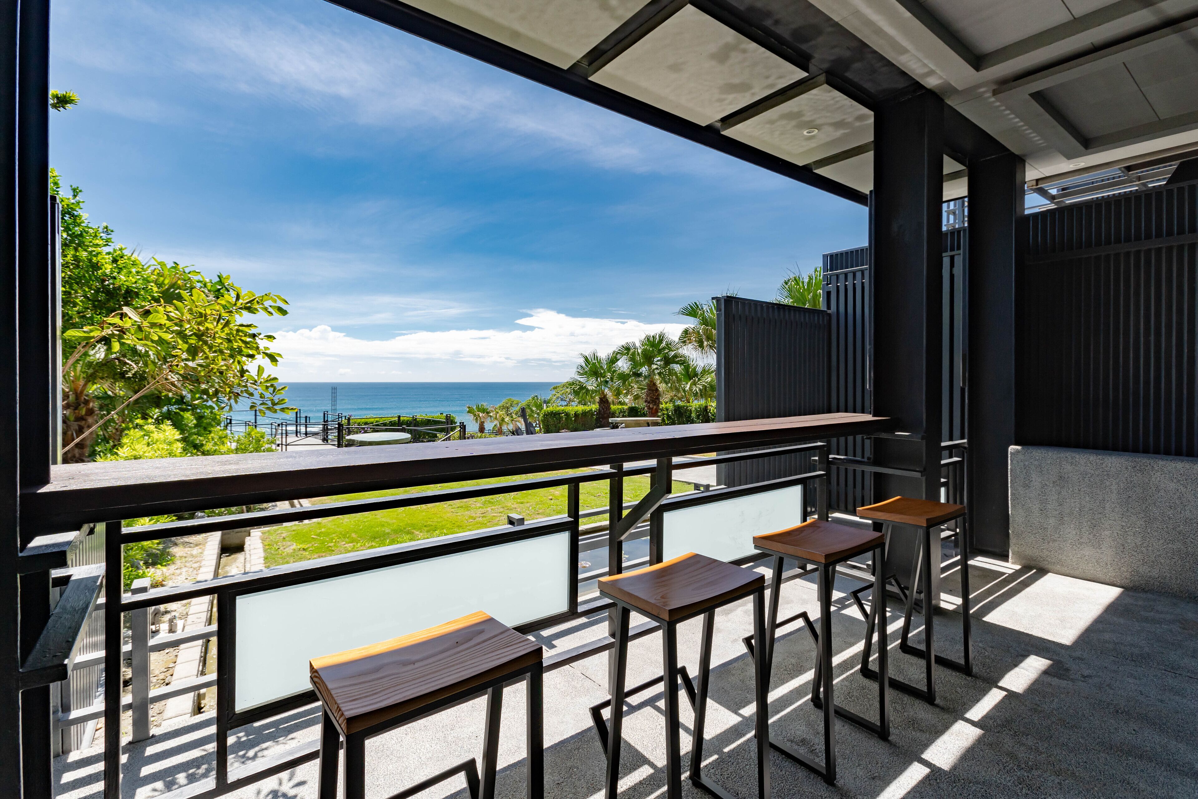 Un balcón con vista al mar, amueblado con mesas y sillas de madera.