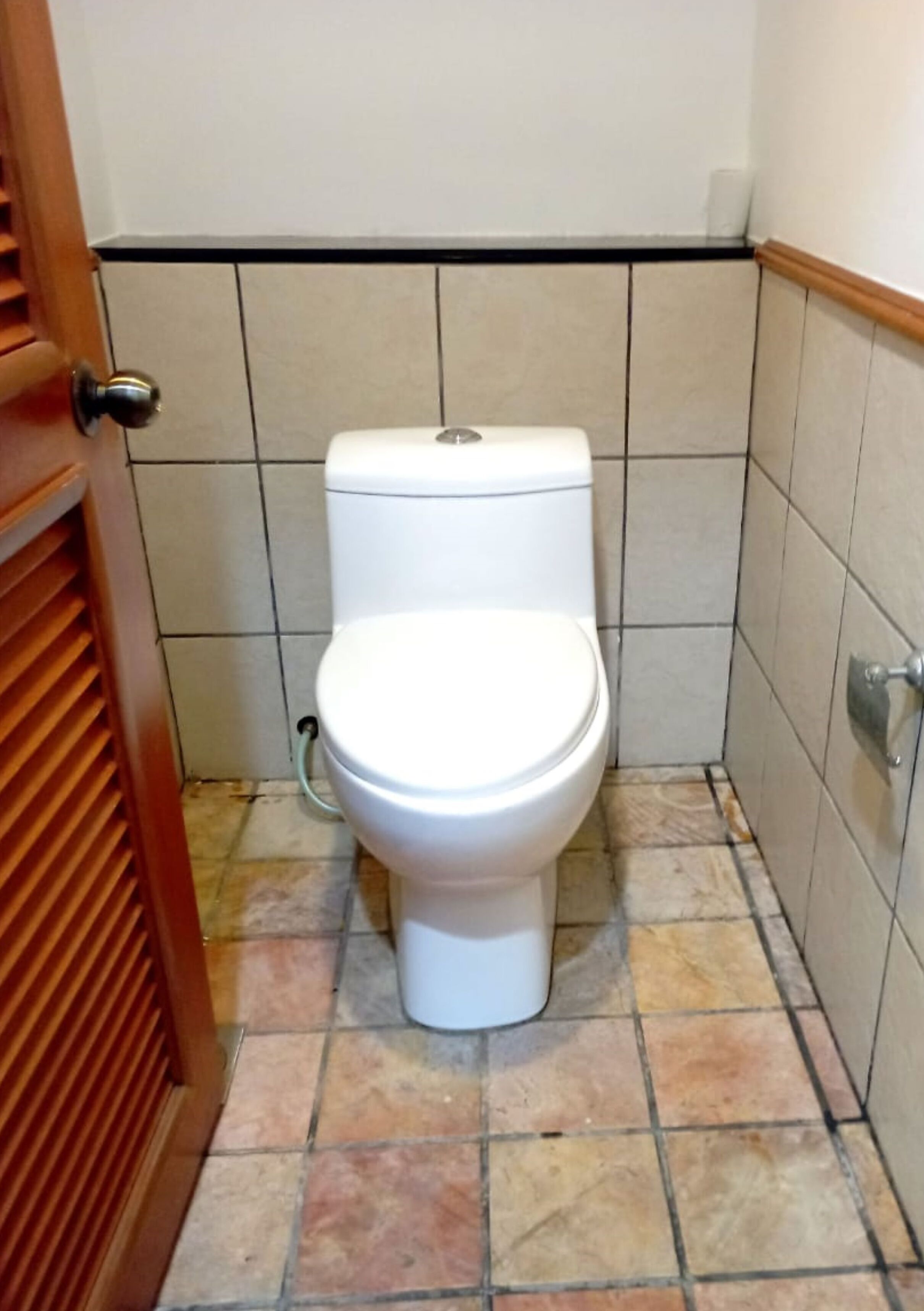 A standard bathroom with a toilet, tiled walls, and a wooden door.