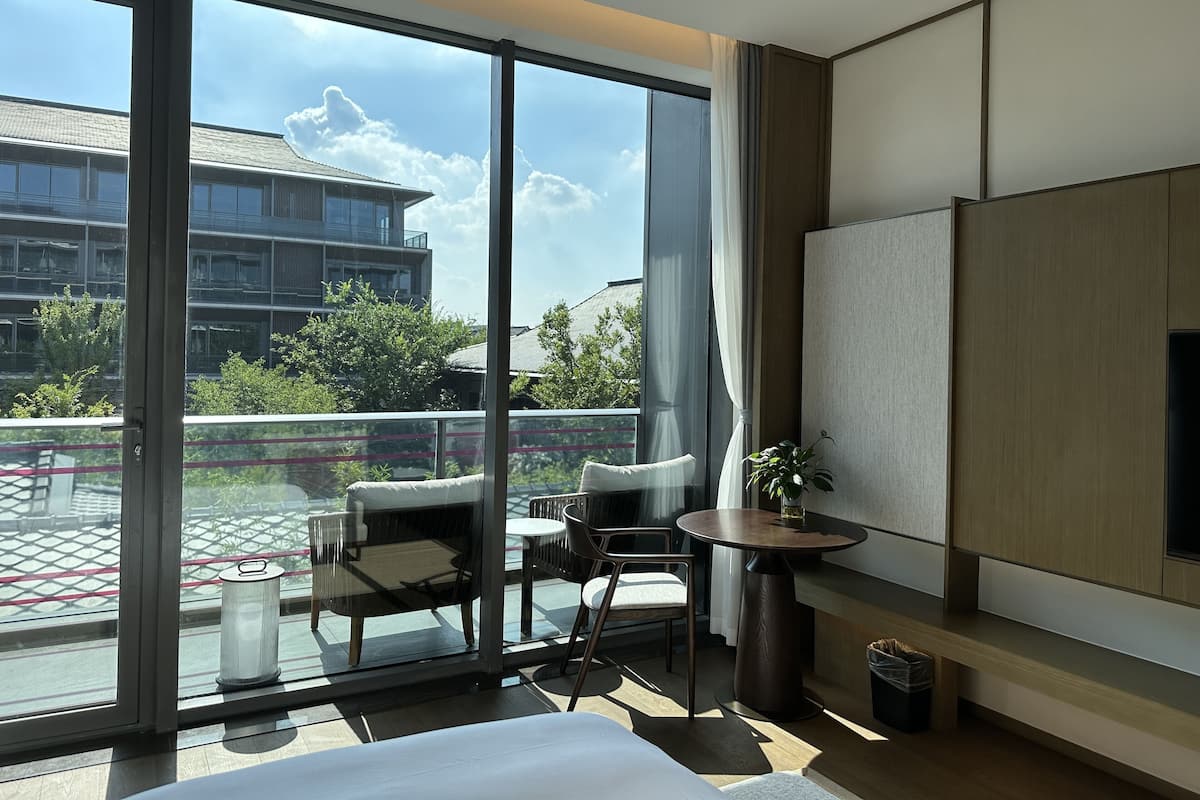 Una habitación de hotel moderna con un balcón grande, una cama, un televisor y una pequeña mesa con sillas.