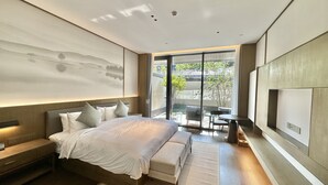 A modern bedroom with a large bed, bedside tables, a seating area with a table and chairs, and a view of the outdoors through large windows. - Blue City Fenghe Resort Hotel (Jiaxing)