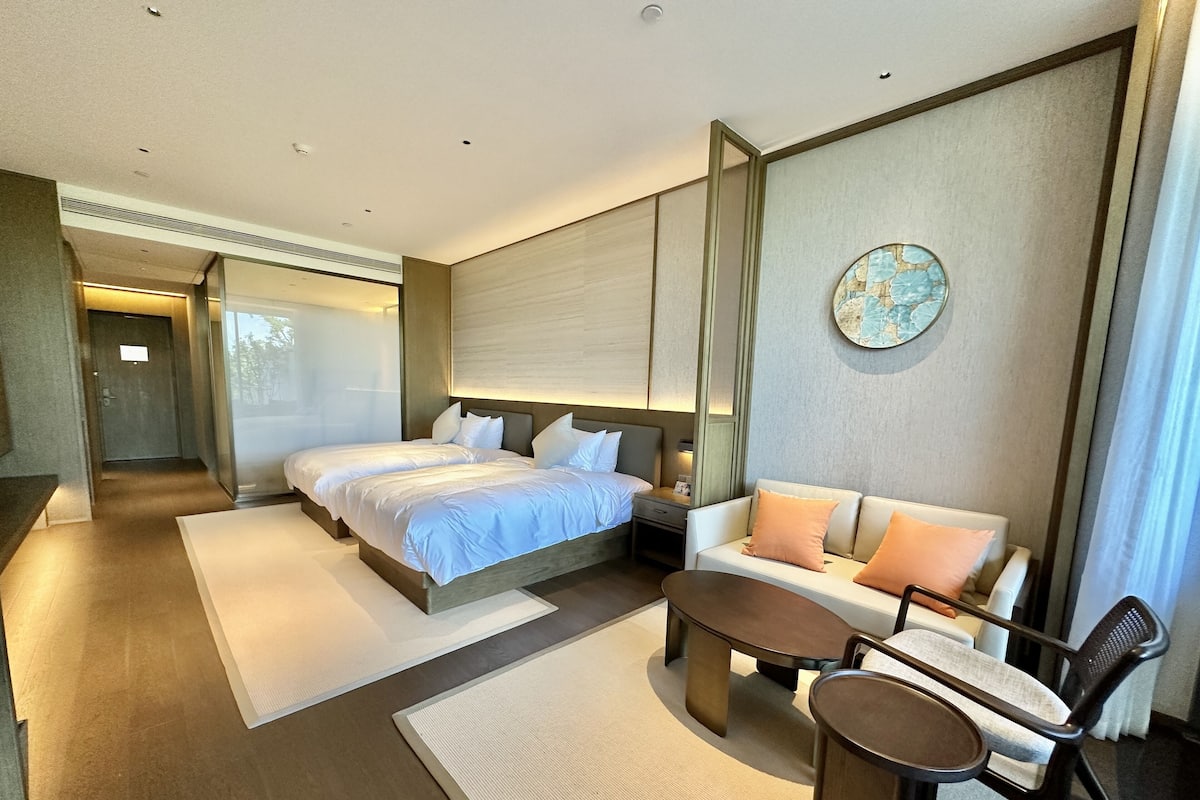 Una habitación de hotel moderna con una cama grande, un sofá, una mesita de centro y una mesita auxiliar pequeña.