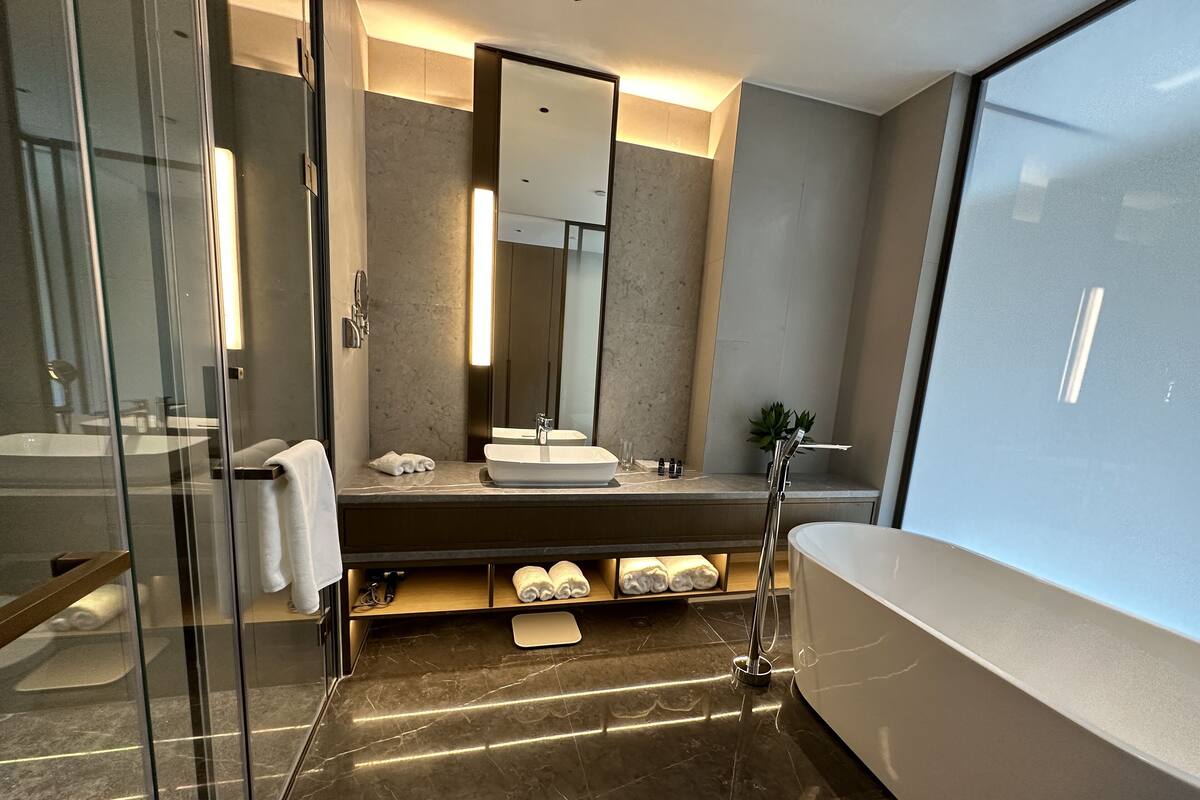 Un baño moderno con cabina de ducha de vidrio, un espejo grande, una bañera y un tocador con lavabo y espacio para toallas.