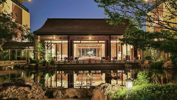 A traditional-style building with a reflective pond in front, wooden railings, and potted plants. - Blue City Fenghe Resort Hotel (Jiaxing)