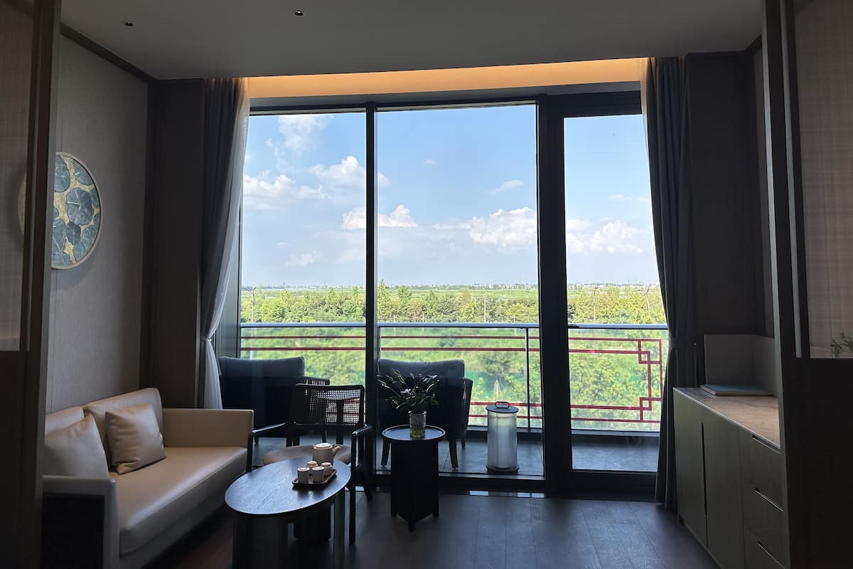 Habitación de hotel moderna con balcón, sofá, una pequeña mesa y vista a zonas verdes.