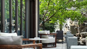 A patio area with outdoor seating, stone walls, and a view of the surrounding greenery. - Blue City Fenghe Resort Hotel (Jiaxing)