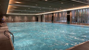 An indoor swimming pool with clear water, surrounded by walls with vertical wooden slats and a modern ceiling design. - Blue City Fenghe Resort Hotel (Jiaxing)
