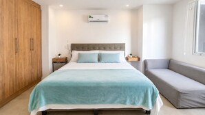 A bedroom with a bed, a grey sofa, a wooden wardrobe, and an air conditioning unit. - Luxury Beachfront Apartment in Chipipe – Stunning Views & Top Amenities (Salinas)