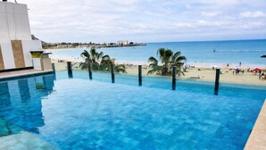 A swimming pool with clear blue water, a beach, and a view of the ocean. - Luxury Beachfront Apartment in Chipipe – Stunning Views & Top Amenities (Salinas)