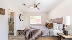 Ein Schlafzimmer mit einem Bett, einem Nachttisch mit Lampe, einem Deckenventilator, einer Uhr und einem Fenster.