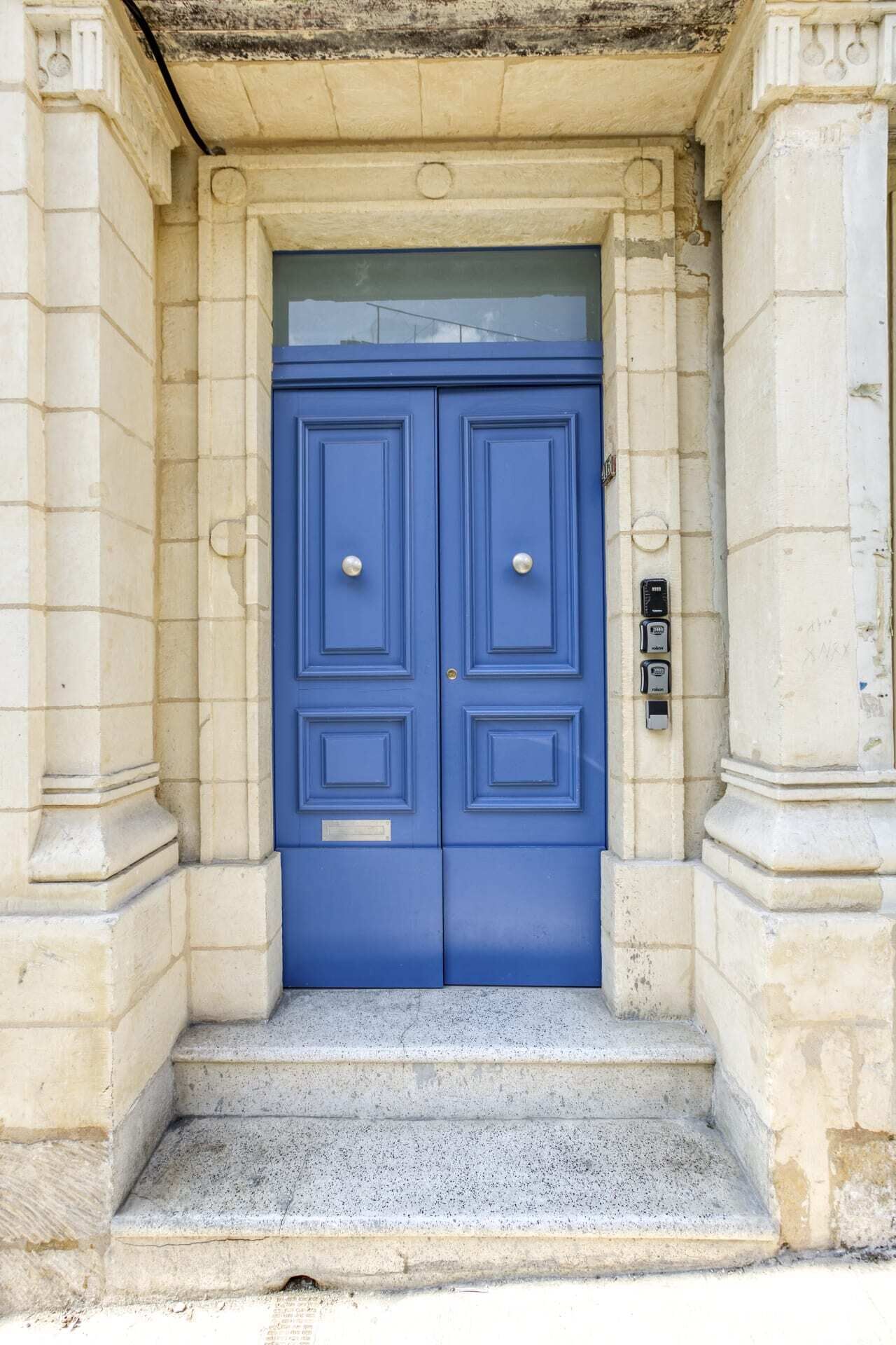 A blue double door with a keypad lock, set in a stone building with a small set of steps leading up to it.