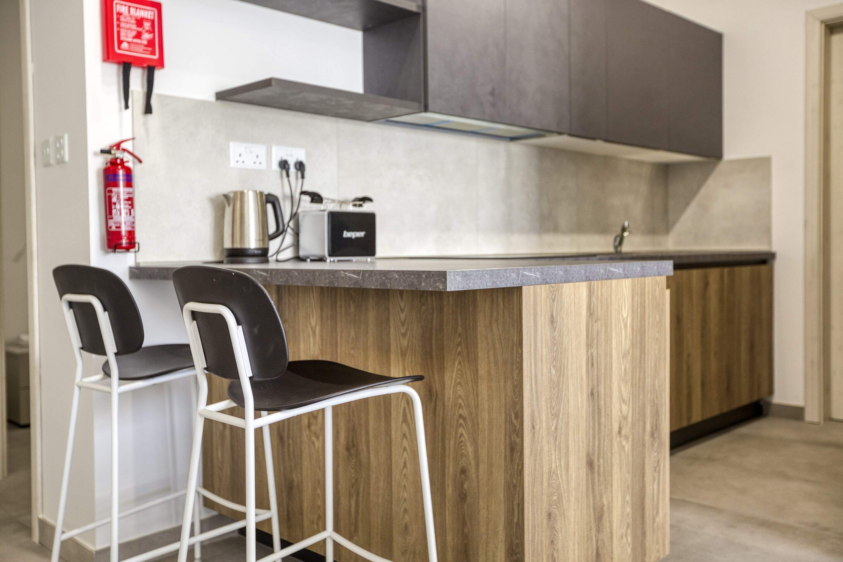 A modern kitchen with a central island, two bar stools, a coffee maker, and a toaster.