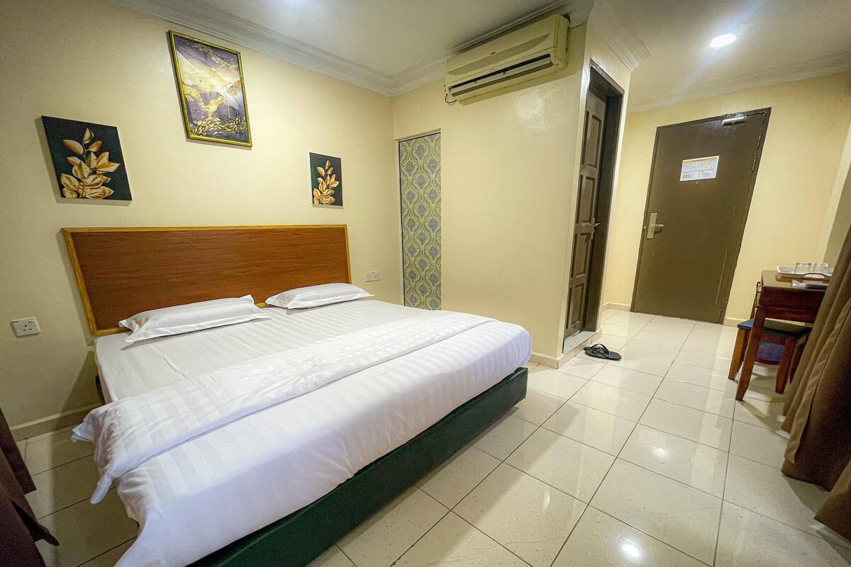 A hotel room with a large bed, a wooden headboard, a wall-mounted air conditioner, and a door with a sign.