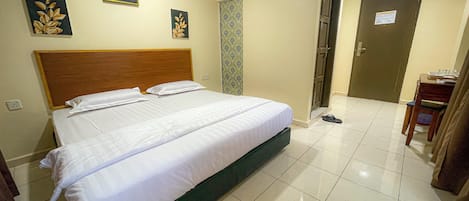 A hotel room with a large bed, a wooden headboard, a wall-mounted air conditioner, and a door with a sign.