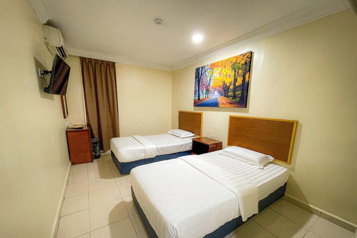 A hotel room with two beds, a painting of a forest, a television, and a window with curtains.