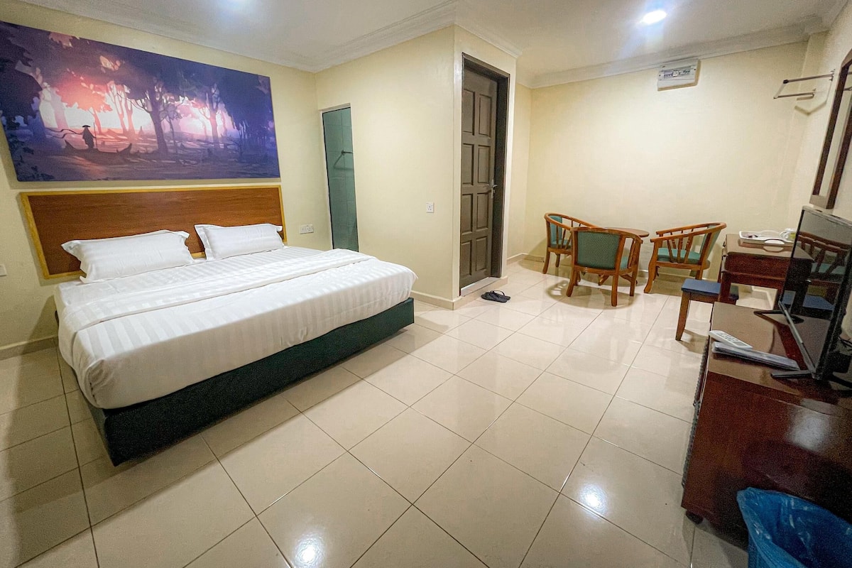 A hotel room with a large bed, a desk with a chair, a television, and a painting on the wall.