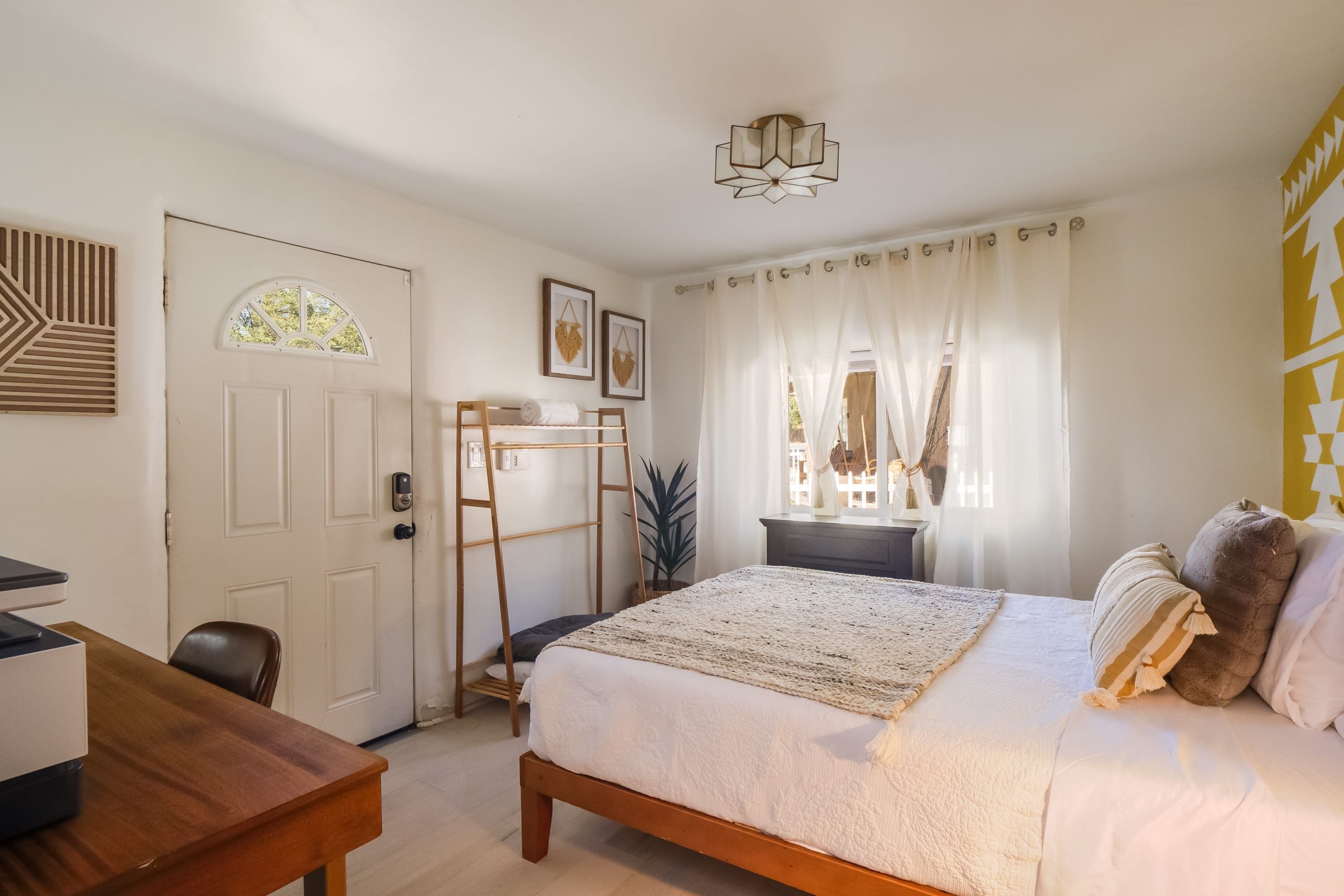 Une chambre à coucher avec un lit, un bureau, une échelle, une porte et une fenêtre avec des rideaux.