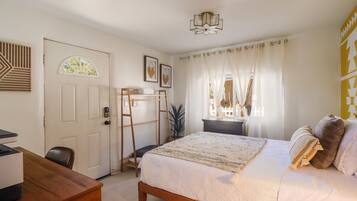 A bedroom with a bed, a desk, a ladder, a door, and a window with curtains.
