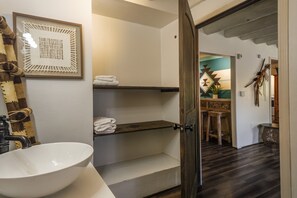 Ein Badezimmer mit einem weißen Waschbecken, einem Handtuchhalter und einem gerahmten Kunstwerk an der Wand.