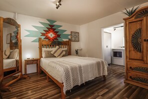 Un dormitorio con una cama de madera, una mesita de noche, un espejo, un armario y una pared con diseños geométricos.