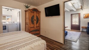 A bedroom with a bed, a wardrobe, a television, and a view into another room.