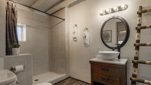 A bathroom with a shower, toilet, sink, and a mirror with lights.